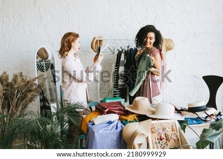 two young woman female caucasian and african students at swap party try on clothes, bags, shoes and accessories, change clothes with each other, second hand for things, zero waste life, eco-friendly Royalty-Free Stock Photo #2180999929
