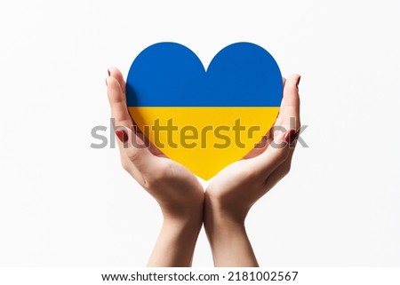 Women hands holding ukraine flag color heart shape paper on white background.