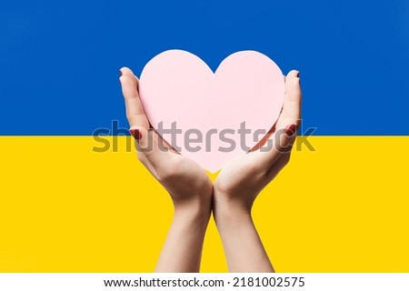 Women hands holding heart shape paper on Ukraine flag color background. Stay with ukraine symbol. Hand heart love gesture with ukrainian flag background.