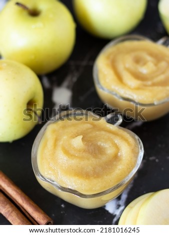 Organic homemade apple puree with a swirl on top in a glass bowl with cinnamon and golden delicious apple on a dark background. Healthy blended baby food, natural applesauce in a dish. Vertical shot. Royalty-Free Stock Photo #2181016245