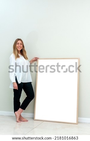 very cheerful young blonde woman in casual clothes holding a large blank poster picture