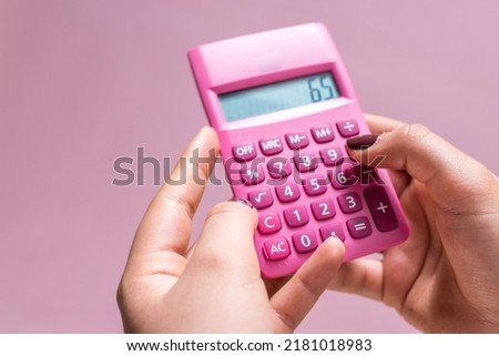 Hands using a pink calculator with white numbers on a pink surface