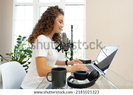 Woman vlogger looking at laptop and recording video with microphone