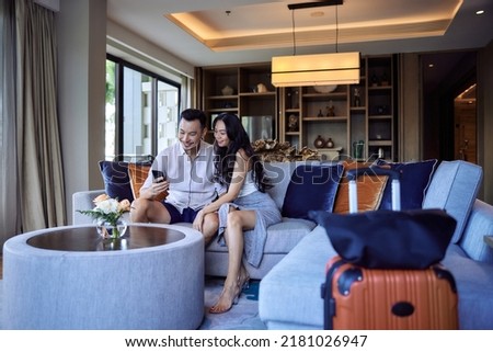 Husband and wife taking selfie photo in hotel room after check-in. Happy young asian couple with suitcases having fun in living room of luxury villa