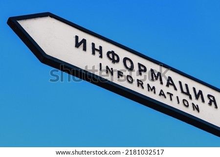 White information sign with Russian and English text is under blue sky