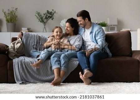 Loving parents and daughter sit on sofa enjoy time together communicating sit on sofa in cozy living room. Offspring upbringing and custody, understanding, good harmonic relations, family bond concept Royalty-Free Stock Photo #2181037861