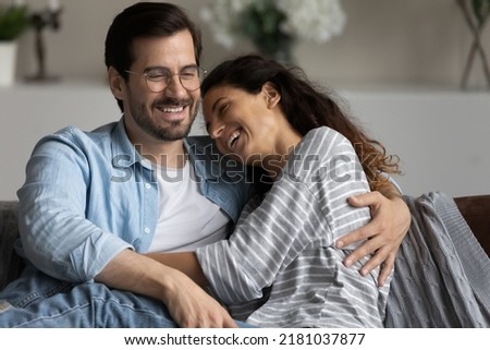 Beautiful couple in love hugging laughing feel carefree, overjoyed enjoy communication sit on sofa, spend romantic date at home, having cheery conversation looking happy. Relations, affection concept Royalty-Free Stock Photo #2181037877