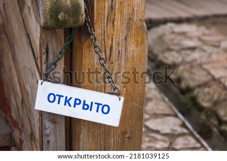 White board with Open text in Russian hanging on vintage wooden door
