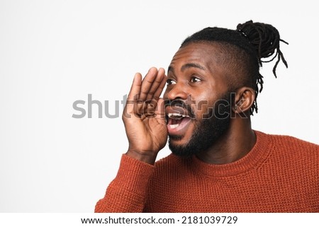 Young african-american man with dreadlocks in red sweater talking loud in hand like loudspeaker telling about discount sale offer isolated in white background Royalty-Free Stock Photo #2181039729
