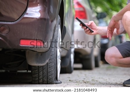 Driver calling road service for assistance having vehicle trouble with punctured flat tire on car parked on roadside