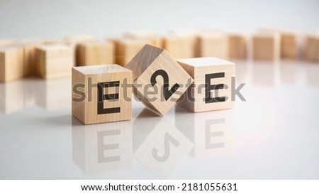 E2E - End to End - an abbreviation of wooden blocks with letters on a gray background. Reflection of the caption on the mirrored surface of the table.