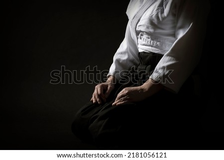 Aikido sitting pose in hakama uniform on black background. Shallow depth of field. SDF. Royalty-Free Stock Photo #2181056121