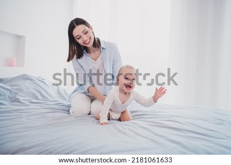 Photo of charming funny small baby mom wear blue shirt holding crawling bed smiling indoors home room Royalty-Free Stock Photo #2181061633
