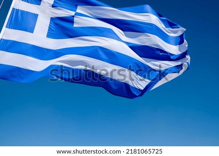 View of the greek flag waving in the air and a blue sky in the background