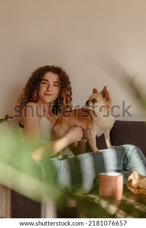 a woman with a chihuahua is sitting on a sofa in a cozy living room. Pets