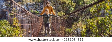 BANNER, LONG FORMAT Father and son tourists on Old rusty bridge. Attraction Long extreme suspension iron bridge across the river Moraca. Sights of Montenegro. Landmark Montenegro