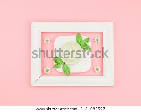 One scoop of vanilla ice cream in a square saucer with mint leaves and chamomile flowers in a white wooden frame on a pink background, flat lay close-up. The concept of ice cream.