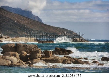 Ocean view of waves crashing against boulders or rocks in the sea in Camps Bay, Cape Town in South Africa. Relaxed and calm landscape view of the sea and mountains against a cloudy overcast sky