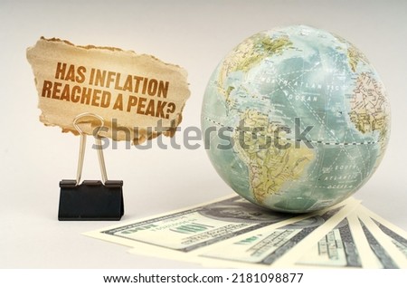 Business concept. On a gray surface, a globe, dollars and a cardboard plate with the inscription - Has inflation reached a peak Royalty-Free Stock Photo #2181098877
