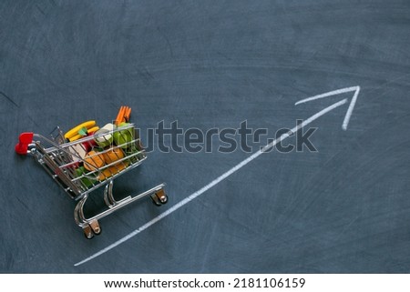Rising food prices.food crisis.Rise in the price of the grocery basket. supermarket trolley with groceries and up arrow on black chalk board background. Food prices.