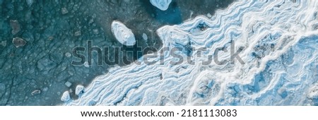 Top view of the icy seashore. Winter aerial photograph of the sea coast. Ice floes in freezing sea water. Nature of the Extreme North and the Arctic. Cold frosty winter weather. Natural background. Royalty-Free Stock Photo #2181113083