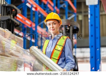 Female worker wrapping boxes in stretch film at warehouse, Worker wrapping stretch film parcel on pallet in factory warehouse