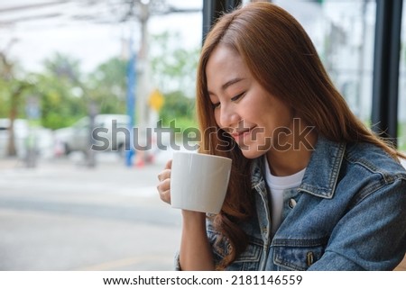 Portrait image of a young asian woman holding and drinking hot coffee in cafe