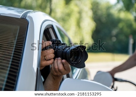 A paparazzi sits in his car and takes pictures of a famous person.  Spy with camera in the car. A private detective, sitting inside the car, taking pictures with the camera.