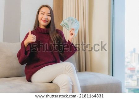 Portrait beautiful young asian woman with a lot of cash and money on sofa in living room interior