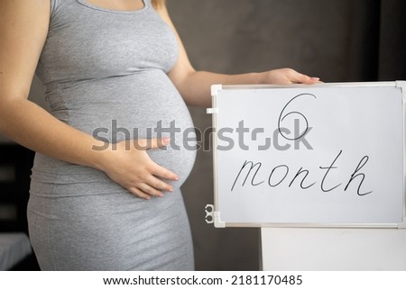 Close up of 6-month-pregnant woman belly holding a whiteboard with text message - 6 month Royalty-Free Stock Photo #2181170485