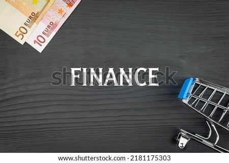 FINANCE - word (text) and euro money on a wooden background, trolley (basket) for goods. Business concept, buying goods and products (copy space).