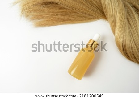 A beauty serum with vitamin C or smoothingoil for hair care lying near the strand of blonde hair