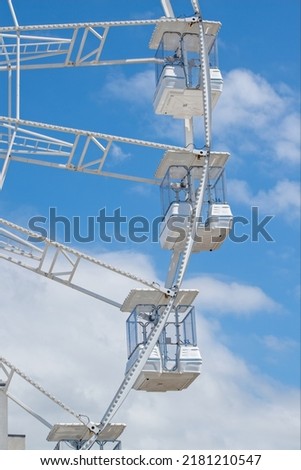 Ferris wheel carriages in white. Blue skies and fluffy clouds contrast the stark white metalwork of the big wheel. a selective picture showing four carriages and only part of the wheel.  
