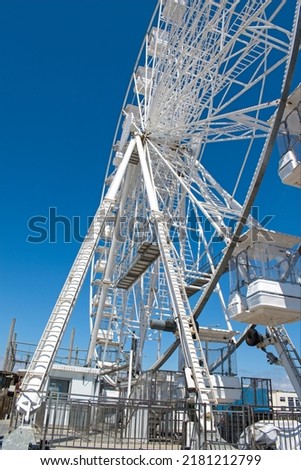 Quirky angled Ferris wheel view. An angled perspective view of a white big wheel fairground ride. Blue sky adds to the summer feel of this interesting picture taken from a unique angle. Leading lines