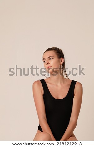 Cute young caucasian woman in black body posing in the studio. Vertical.