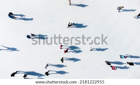 Many people are skating on a white outdoor ice rink in the city on a sunny winter day. Shadows of people skating on the surface of a white ice rink. Aerial drone view. Top view. Lifestyle, sport, rest Royalty-Free Stock Photo #2181222955
