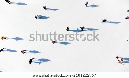 Many people are skating on a white outdoor ice rink in the city on a sunny winter day. Shadows of people skating on the surface of a white ice rink. Aerial drone view. Top view. Lifestyle, sport, rest Royalty-Free Stock Photo #2181222957