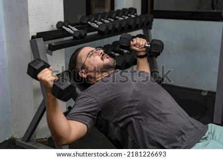 A man in his late 30s makes a comeback at the gym. Doing incline dumbbell flyes with a relatively light weight. A dad getting back in shape. Royalty-Free Stock Photo #2181226693