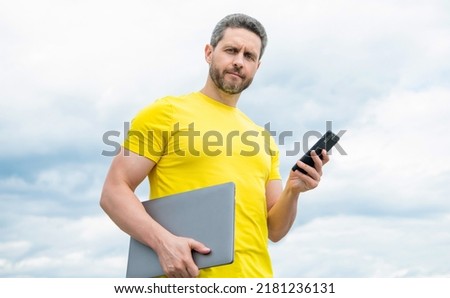 man with laptop chatting on smartphone on sky background