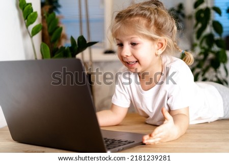 Smiling little Caucasian girl has a video call remote classroom with a teacher using a laptop, happy little child greeting with a tutor, learning online on a computer, home learning concept