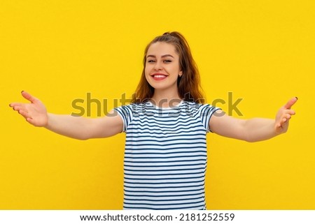 Come into my arms. Portrait of friendly and cute charming girl stretching hands and looking forward with happy smile to cuddle and welcome guests, standing in striped t shirt over yellow background