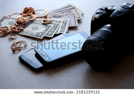 Many expensive golden jewerly rings, earrings and necklaces with big amount of US dollar bills close to smartphones and digital slr camera. Pawn shop concept Royalty-Free Stock Photo #2181259131