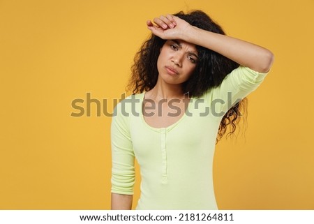 Exhausted fatigued sad african american young brunette woman 20s wears green shirt hand on forehead isolated on yellow background studio portrait. Healthy lifestyle sick ill disease treatment concept