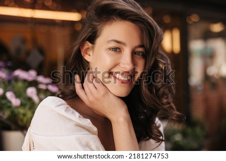Close-up of nice young caucasian woman in good mood looking at camera on blurred background. Brunette with wavy hair wears dress summer. Lifestyle, different emotions, leisure concept. Royalty-Free Stock Photo #2181274753