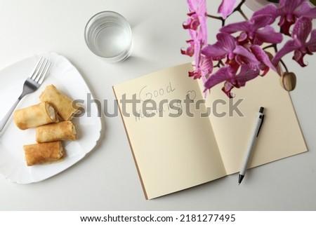 Notebook with inscription Good Morning, stuffed crepes and glass of water near beautiful blooming orchid on white table, flat lay