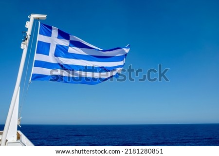Huge greek flag of a ferry boat waving in the wind and the Aegean Sea in the background