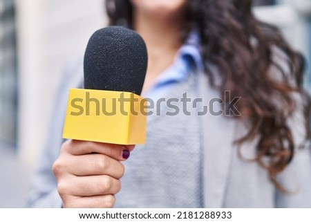 Young hispanic woman reporter working using microphone at street Royalty-Free Stock Photo #2181288933