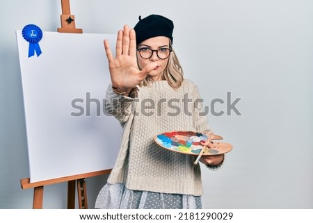 Beautiful caucasian woman drawing with palette on easel stand winner first place with open hand doing stop sign with serious and confident expression, defense gesture 