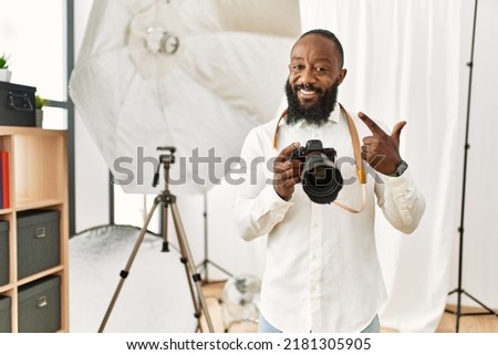 African american photographer man working at photography studio cheerful with a smile on face pointing with hand and finger up to the side with happy and natural expression 
