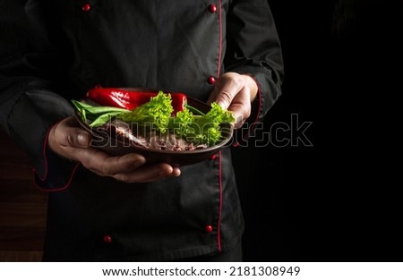 The chef presents his dish on a plate of sliced baked steak and vegetables. Space for hotel menu or recipe on dark background